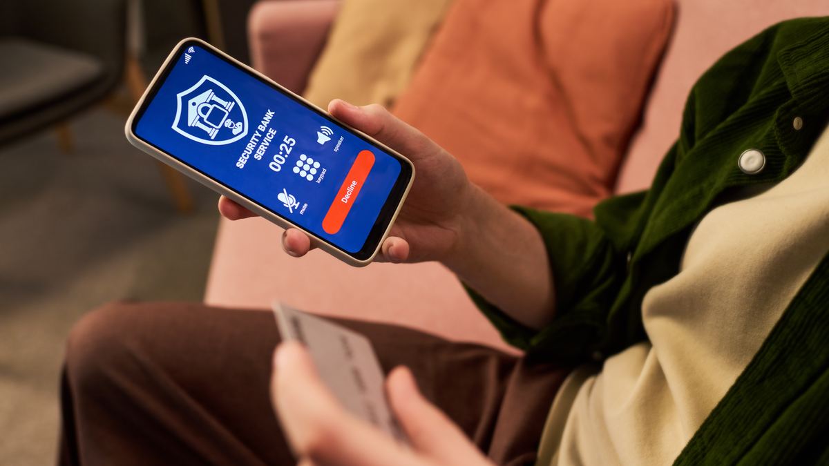 A person holding a bank card and a smartphone showing an alert about an unknown account transaction.