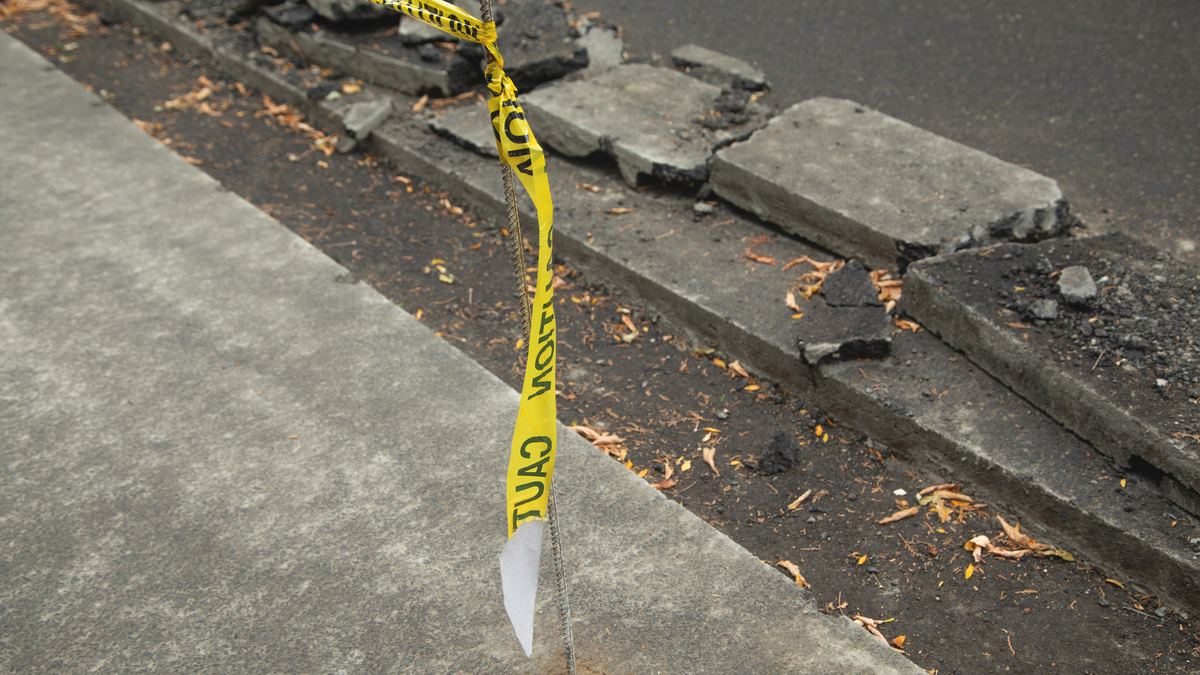 Sunken paving slabs and a hole in a city pavement next to a pedestrian crossing, with the area cordoned off with tape.