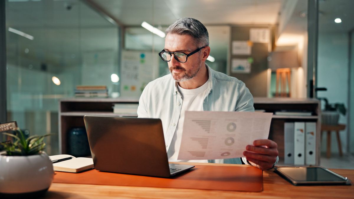 The manager of a small company checking a Commercial Register extract on a laptop next to a folder of old annual financial statements.